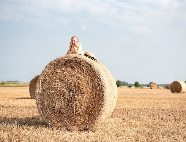 Bambina divertirsi in un campo di grano in una giornata estiva. Bambino che gioca al campo di balle di fieno durante il periodo del raccolto.