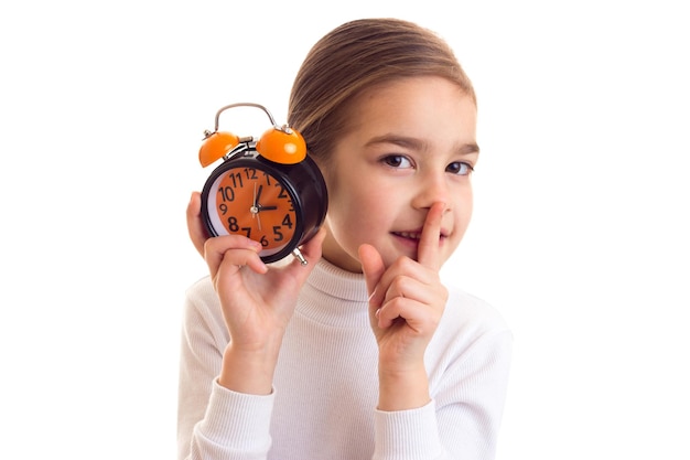 Bambina dolce con una lunga coda di cavallo marrone in camicia bianca e gonna nera che tiene l'orologio arancione