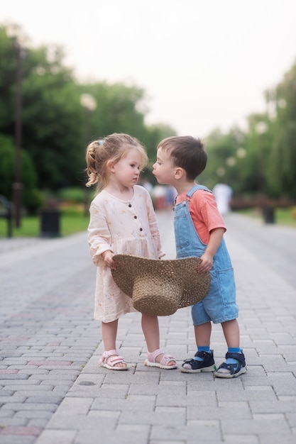 bambina e bambino si abbracciano e si baciano stanno in piedi al centro del vicolo verde e tengono in mano un cappello di paglia straw