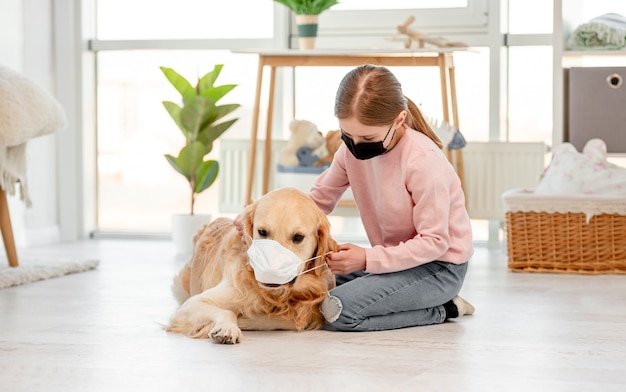 Bambina e cane golden retriever indossando maschere a casa in tempo di pandemia