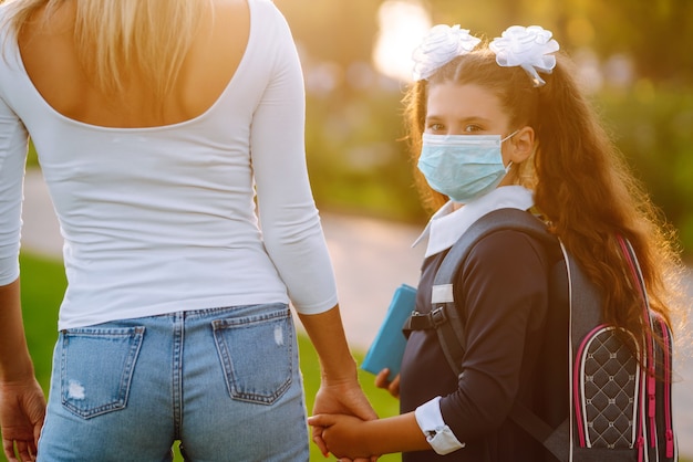 Bambina e mamma in maschera medica durante covid-19. Mamma e figlia vanno a scuola.