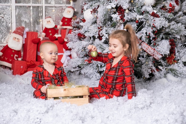 Bambina e neonato che giocano con le palle di natale nella stanza decorata di natale. buon natale concetto.