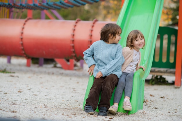 bambina e ragazzo carini nel parco per bambini che si divertono e gioiscono mentre giocano nel parco giochi in una giornata nuvolosa autunnale