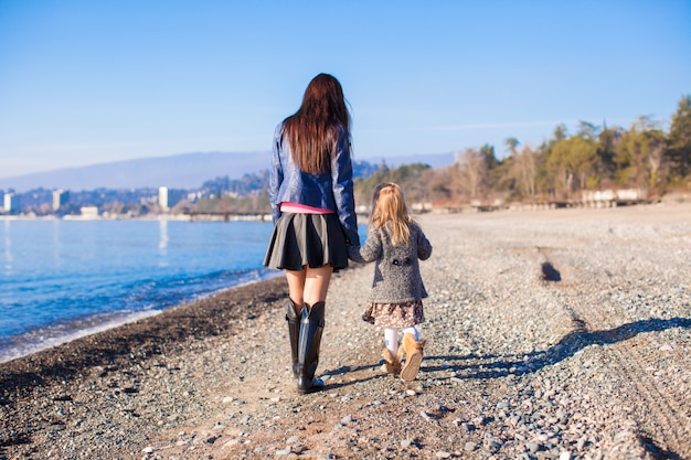 Bambina e sua madre che camminano sulla spiaggia nel giorno soleggiato di inverno