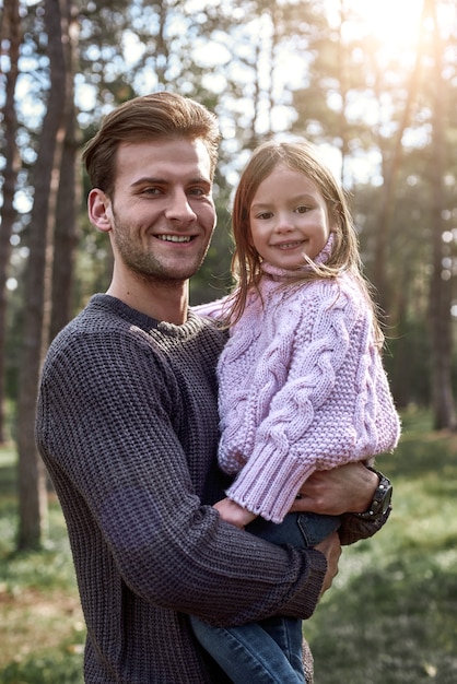 Bambina e suo padre nella foresta. La ragazza sta cercando il padre. Il giovane indossa un maglione scuro, la ragazza indossa un maglione rosa brillante