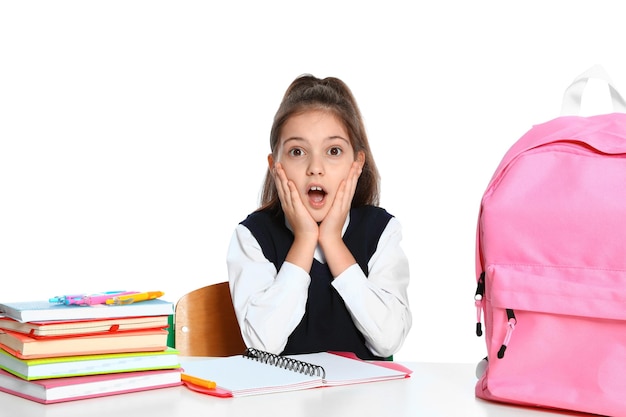 Bambina emotiva in uniforme con cancelleria scolastica alla scrivania su sfondo bianco