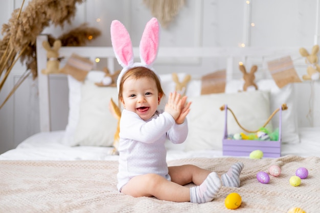 Bambina felice carina in orecchie da coniglio sul letto a casa con un coniglio e uova dipinte concetto pasquale divertente Pasqua bambino sta aspettando le vacanze e gioendo