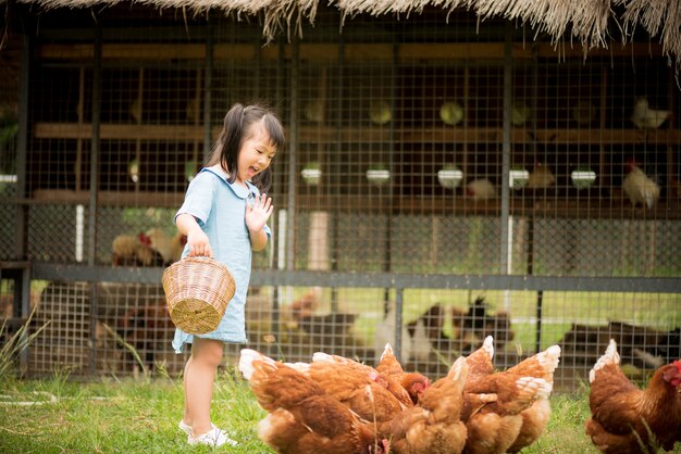 Bambina felice che alimenta i polli davanti all&#39;azienda agricola di pollo.