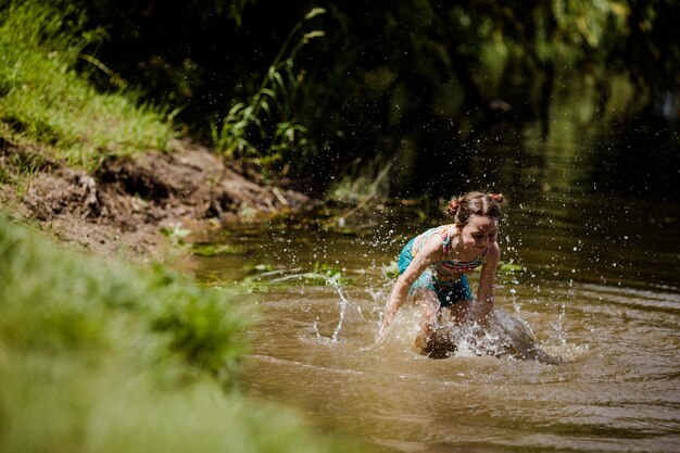 Bambina felice che cade nel lago in estate in una giornata di sole