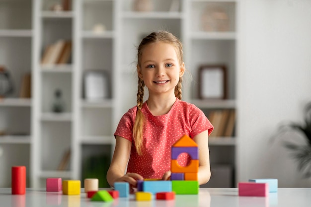Bambina felice che gioca con i mattoni di legno colorati e sorride alla macchina fotografica