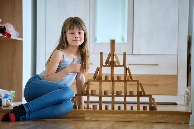 Bambina felice che gioca impilando blocchi giocattolo in legno in una struttura a pelo alto Controllo del movimento delle mani e costruzione del concetto di abilità computazionali