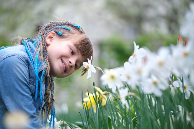 Bambina felice che gioca nel giardino estivo godendo di un dolce profumo di fiori di narciso bianco in una giornata di sole