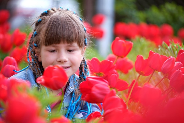 Bambina felice che gode del dolce profumo dei fiori di tulipano rosso nel giardino estivo