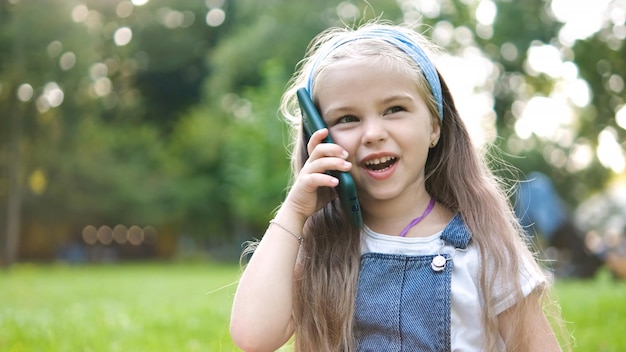 Bambina felice che ha conversazione parlando al cellulare nel parco estivo