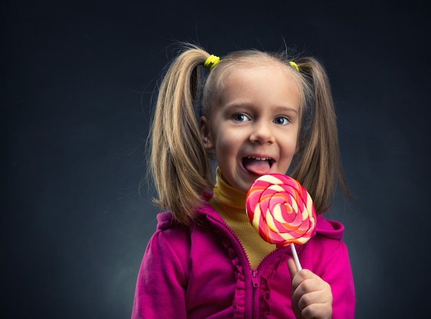 Bambina felice che mangia lecca-lecca su una superficie scura