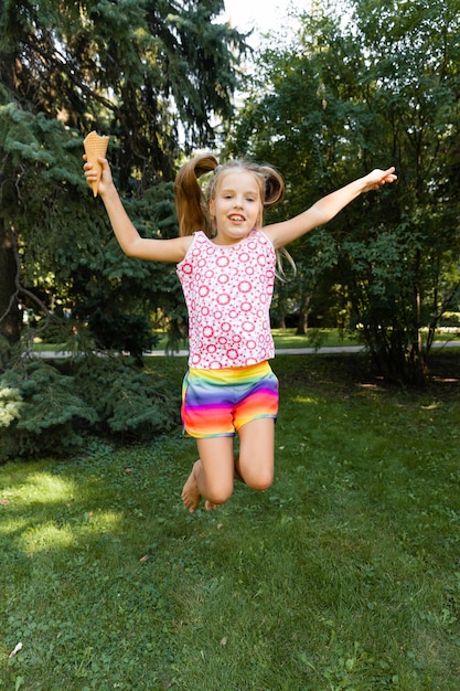 Bambina felice che salta nel parco. bambina che mangia il gelato e si diverte in città.