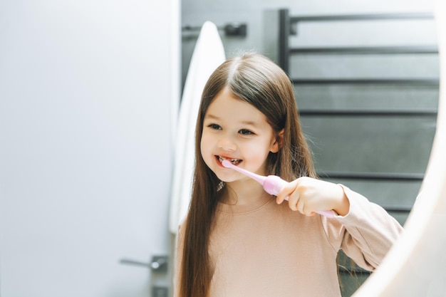 Bambina felice che si lava i denti davanti allo specchio del bagno Igiene mattutina