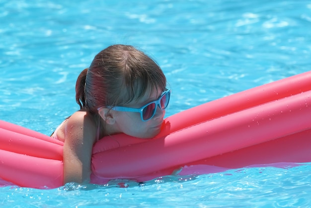 Bambina felice che si rilassa sul materasso gonfiabile in piscina nelle soleggiate giornate estive durante le vacanze tropicali Concetto di attività estive