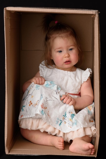 Bambina felice che si siede in una scatola di cartone e che si diverte