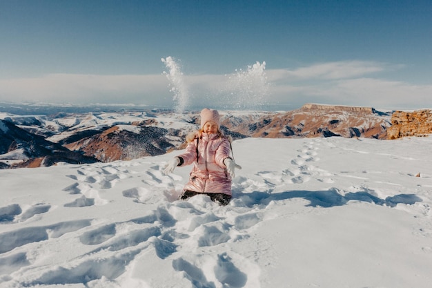 Bambina felice che si siede nella neve e che vomita neve con gioia. concetto invernale