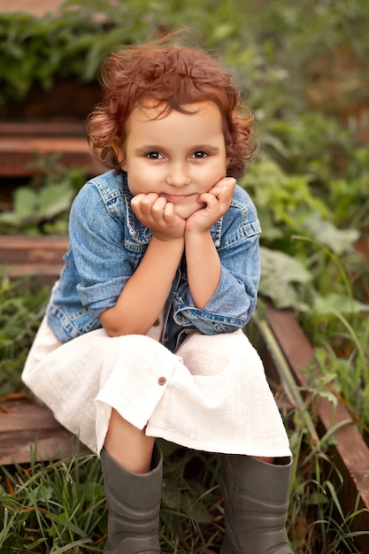 Bambina felice che si siede su una scala di legno. Vita di campagna estiva.