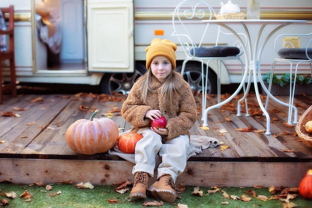 Bambina felice che si siede sul portico di casa con le zucche e che decora la casa per Halloween