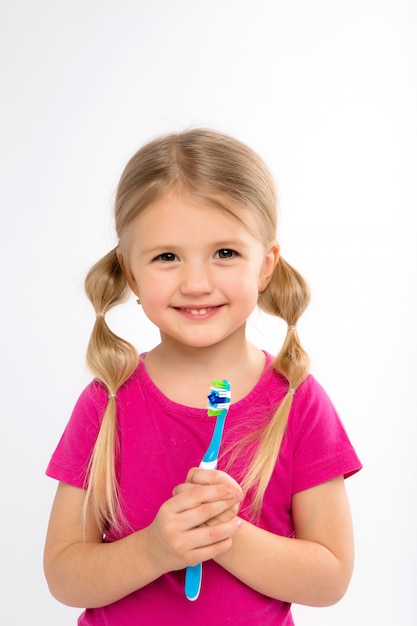 Bambina felice che sta con lo spazzolino da denti isolato su bianco.