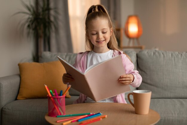 Bambina felice che tiene il libro di schizzi che disegna a casa