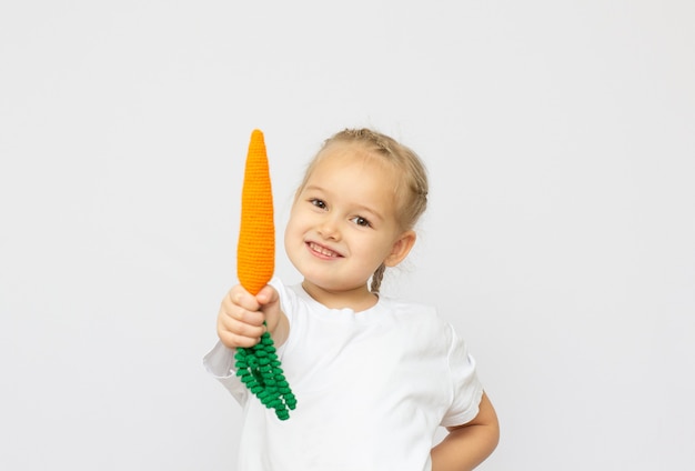 Bambina felice che tiene un knitt carote. Concetto di cibo sano.