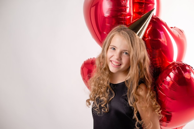 Bambina felice con bracciata di palline a forma di cuori e un berretto per il suo compleanno.