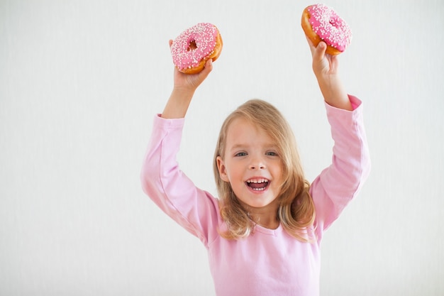 Bambina felice con i capelli biondi, giocando e gustando ciambelle con glassa rosa alla celebrazione di hanukkah