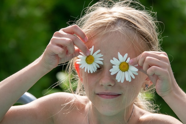 Bambina felice con i fiori della margherita sugli occhi. Estate