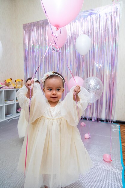 Bambina felice con il bellissimo vestito che gioca con i palloncini durante il suo compleanno