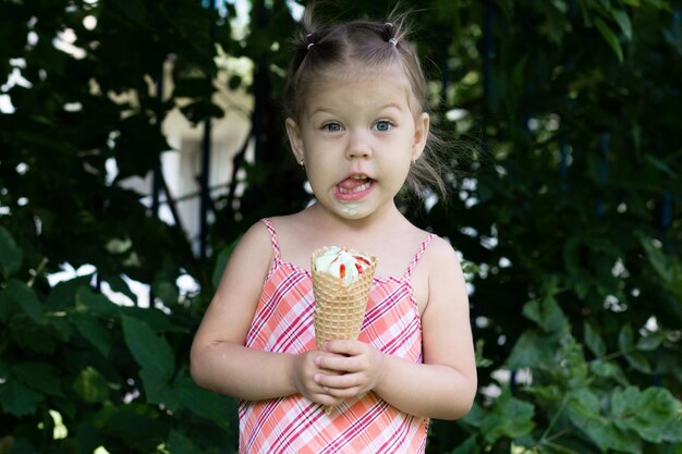 Bambina felice con il corno di gelato della cialda che guarda l'obbiettivo nel parco estivo