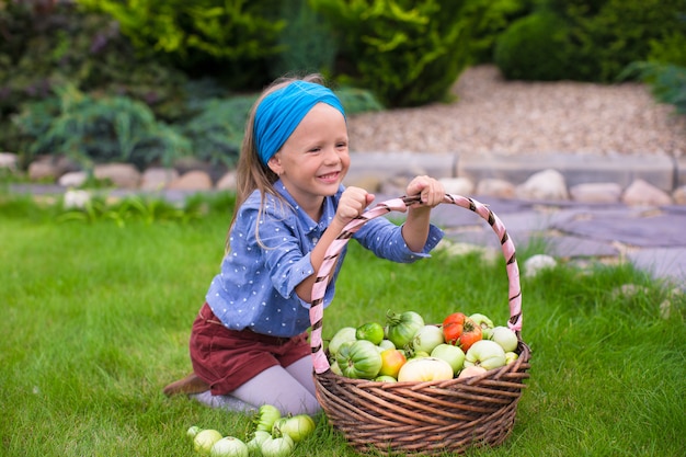 Bambina felice con il raccolto di autunno del pomodoro in cestini