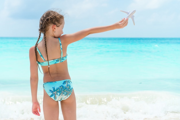 Bambina felice con l'aeroplano giocattolo in mani sulla spiaggia di sabbia bianca.