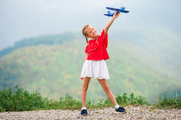 Bambina felice con l'aeroplano giocattolo nelle mani in montagna