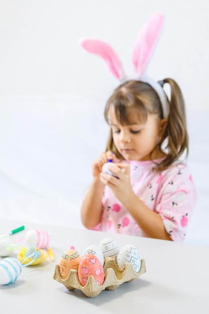 Bambina felice con le orecchie del coniglietto che dipinge l'uovo con la penna di fibra che si prepara per il giorno di Pasqua felice