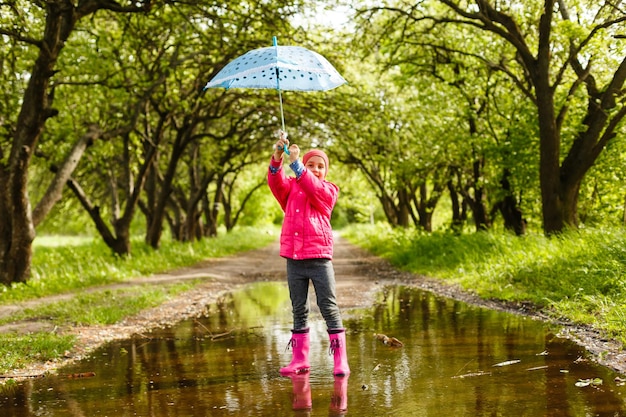 bambina felice con un ombrello e stivali di gomma nella pozzanghera in una passeggiata autunnale