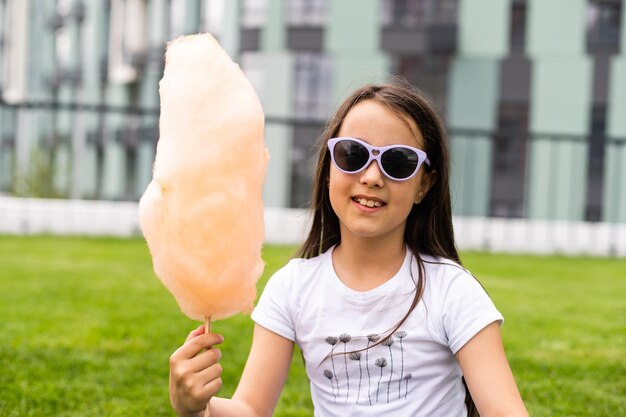 Bambina felice con zucchero filato dolce nel parco estivo.