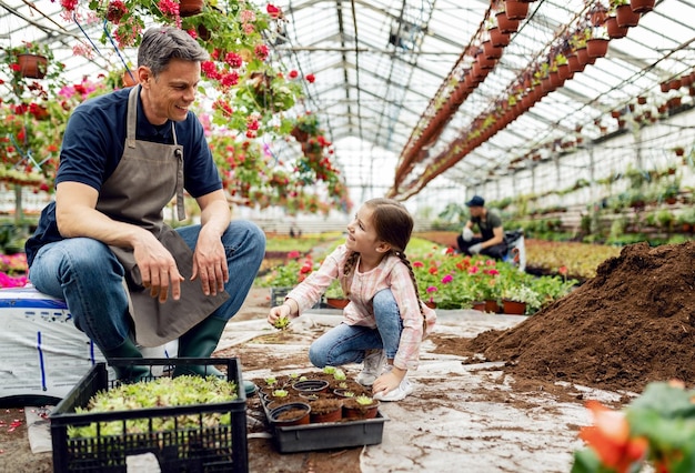 Bambina felice e suo padre che piantano fiori insieme e parlano in una serra