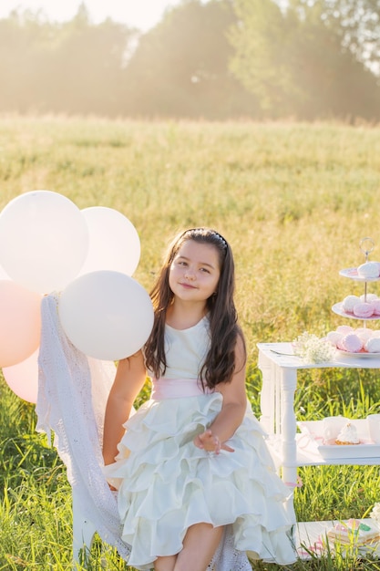 Bambina felice in abito bianco con torta di compleanno in campo estivo