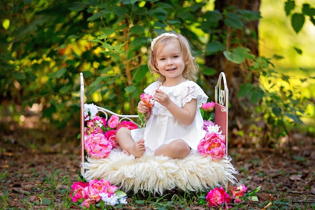 Bambina felice in abito da principessa retrò a letto con fiori rosa all'aperto in estate
