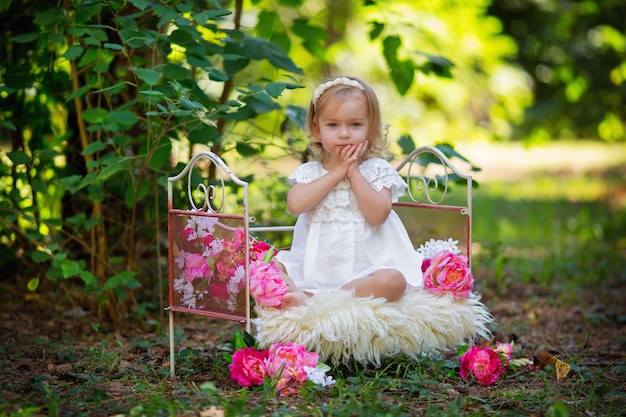 Bambina felice in abito da principessa retrò a letto con fiori rosa all'aperto in estate