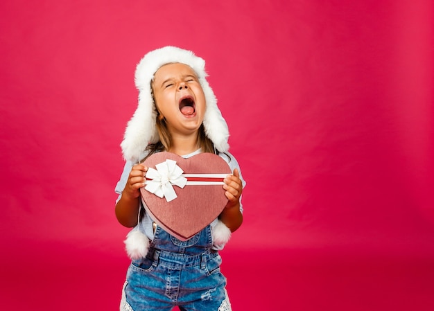 Bambina felice in cappello invernale con regalo di Natale su sfondo rosa