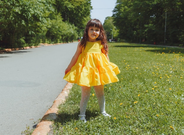 Bambina felice in un abito estivo giallo corre sull'erba nel parco