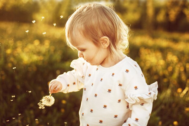 bambina felice in un campo con un dente di leone in mano