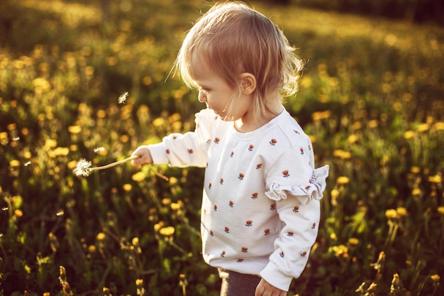 bambina felice in un campo con un dente di leone in mano