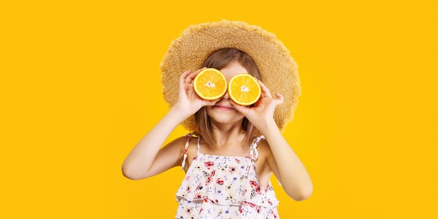 Bambina felice in un cappello di paglia che tiene un'arancia su uno sfondo giallo con spazio per il testo