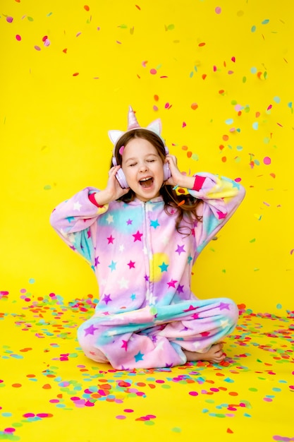 Bambina felice in un unicorno Kigurumi su uno sfondo giallo